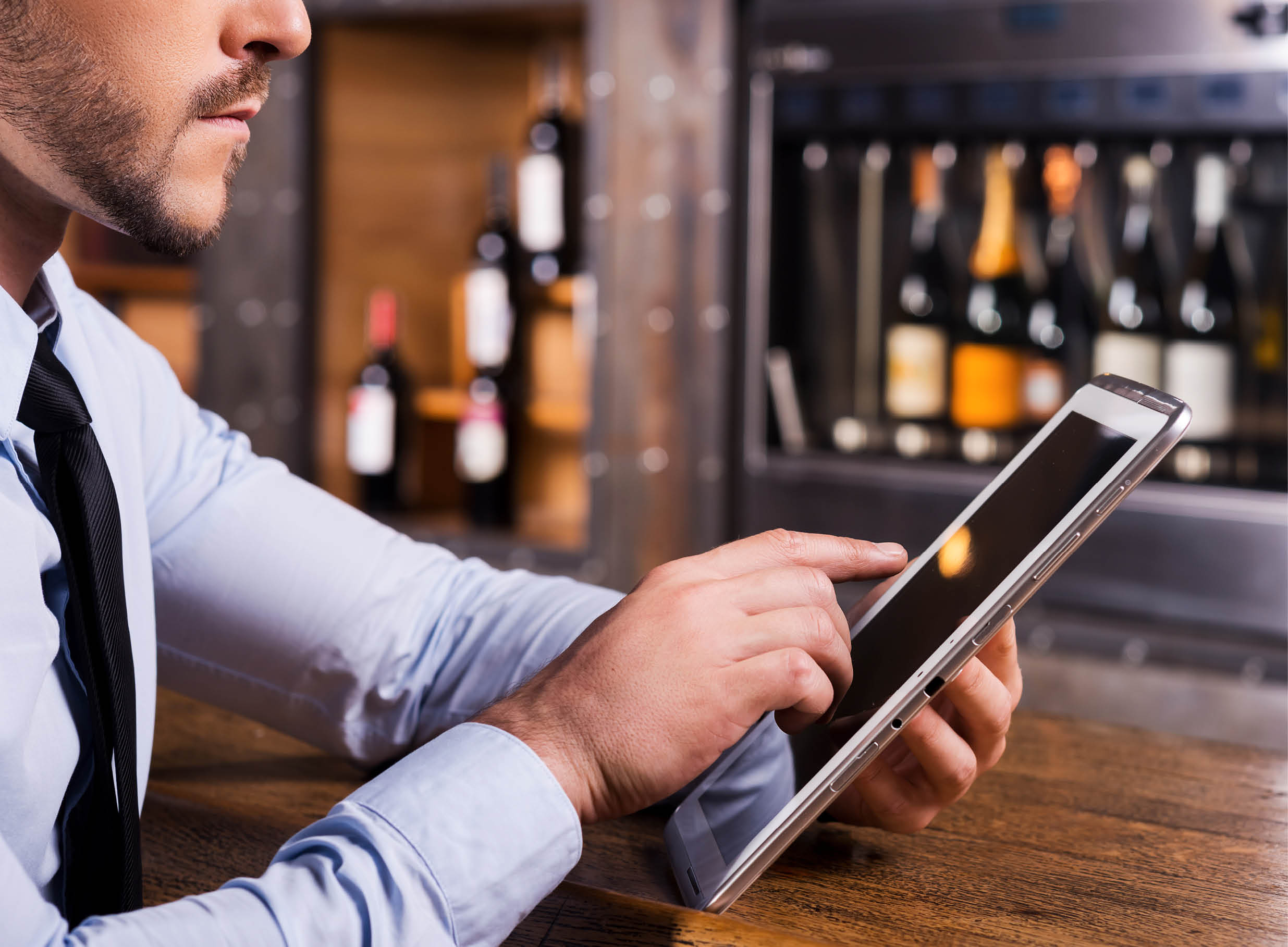 Surfing web in bar. Close-up of man in shirt and tie working on digital tablet while sitting at the bar counter 