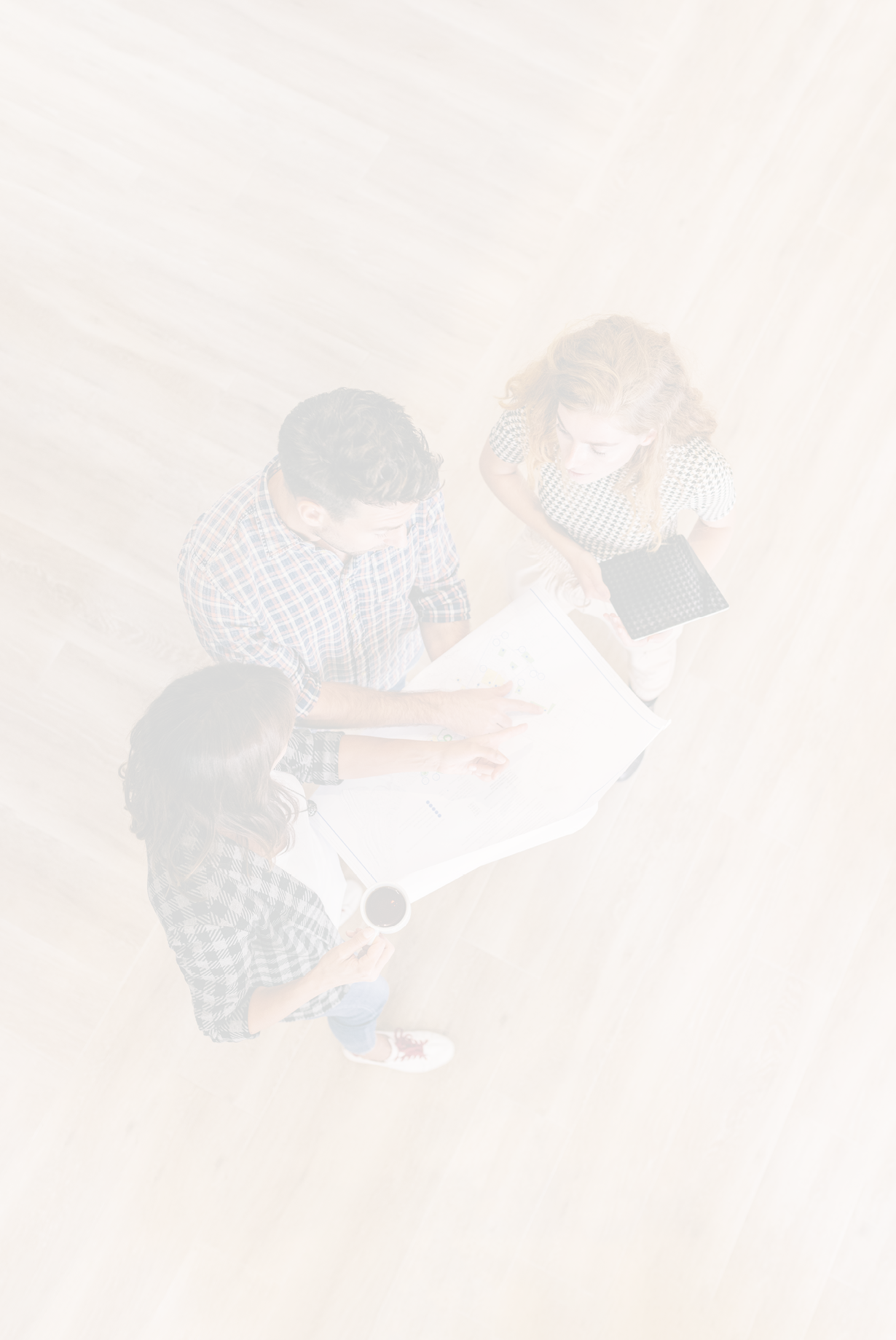 Creative architects on casual meeting reviewing blueprints standing on a wooden floor. Top view.