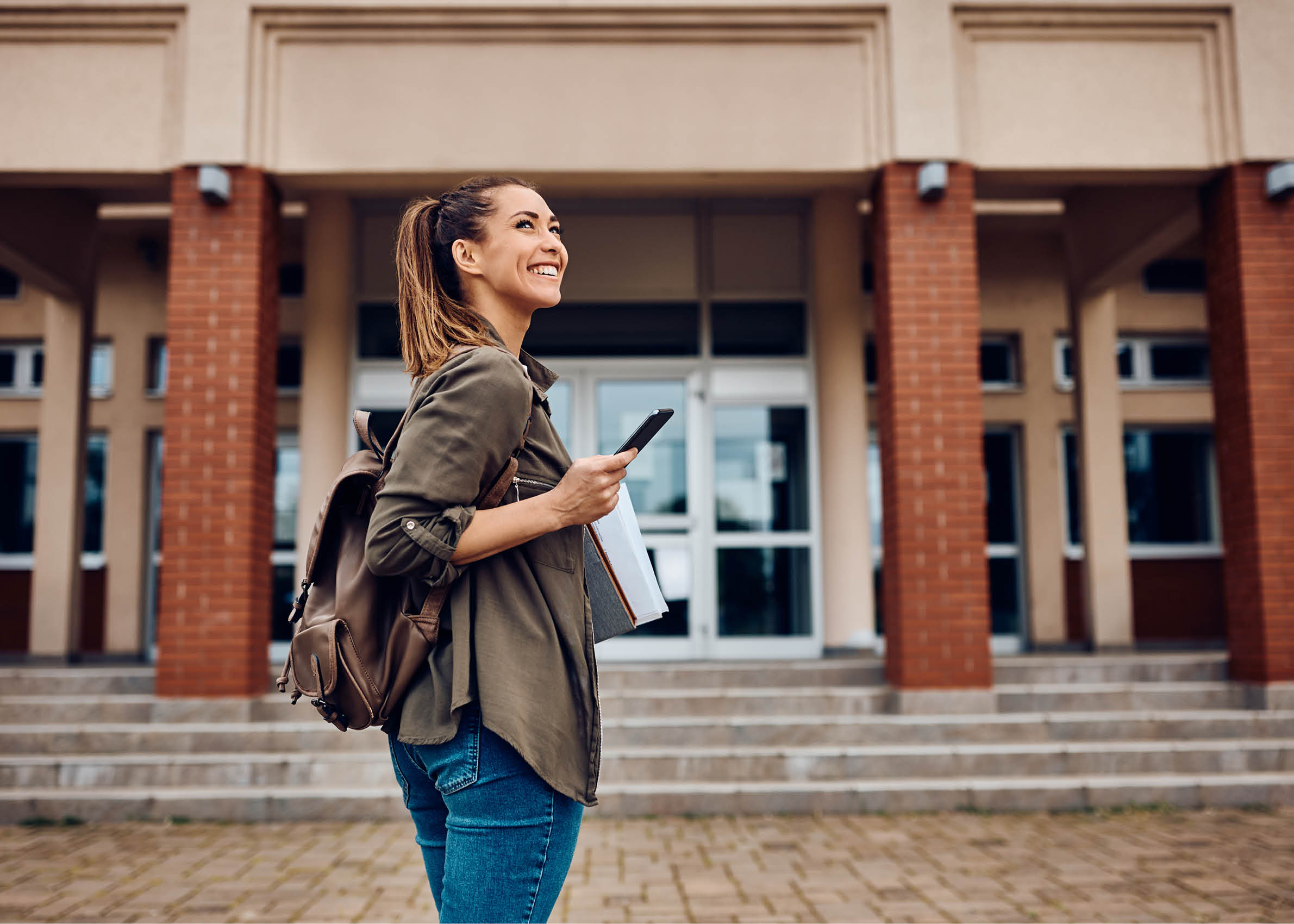 Happy female student texting on smart phone while going to lecture at the university. Copy space. 
