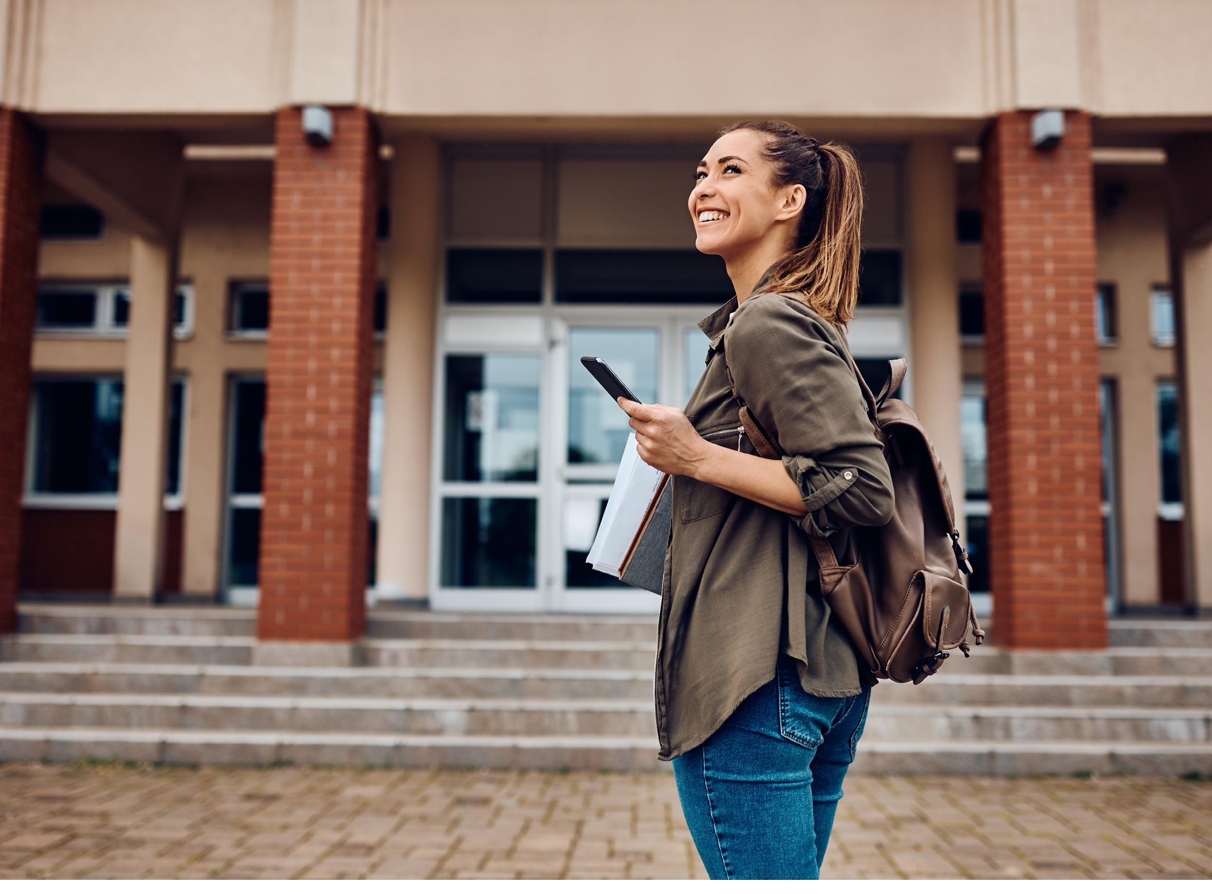 Happy female student texting on smart phone while going to lecture at the university. Copy space. 