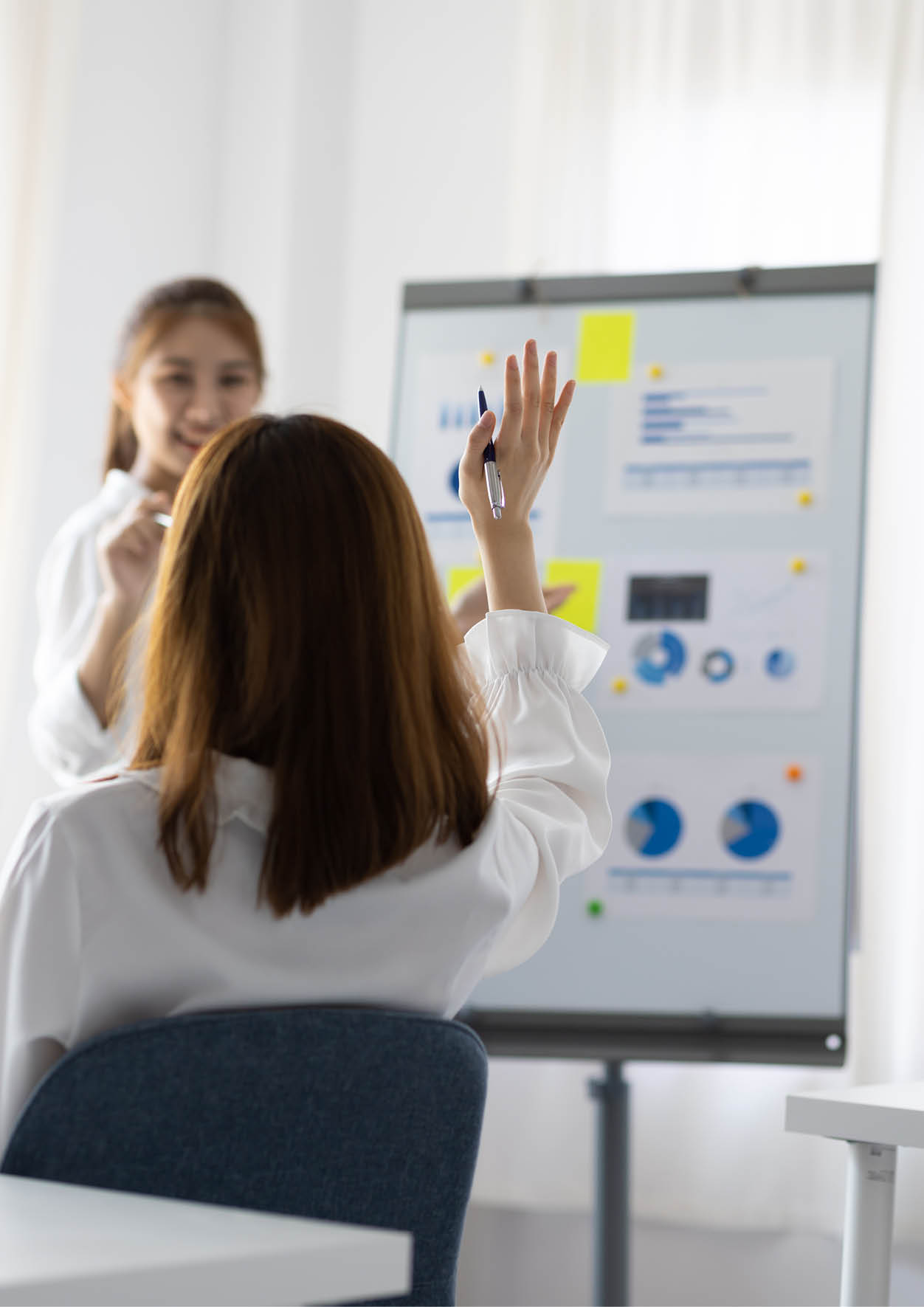 Colleagues raise their hands to ask questions during a business meeting.