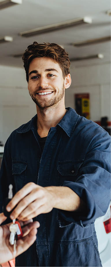 Car mechanic passing car keys to the car owner after repairing his vehicle. Mechanic giving car key to customer after servicing at garage.