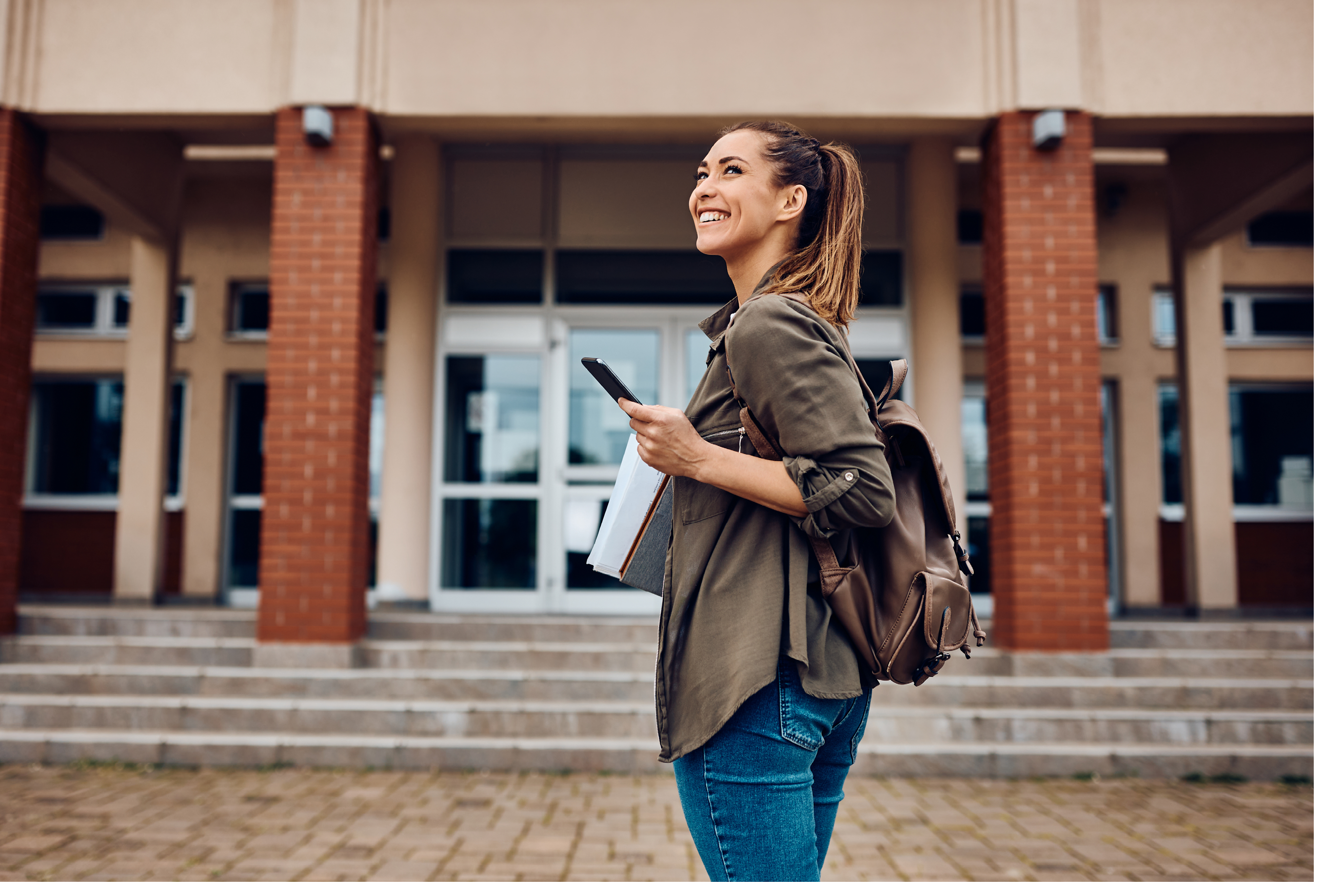 Happy female student texting on smart phone while going to lecture at the university. Copy space. 