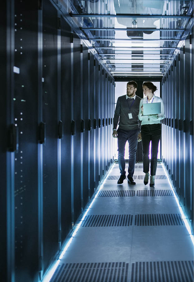 Female IT Technician and Male Server Engineer Talk and Discuss. They are in Working Data Center full of Rack Servers. Woman Holds Laptop.