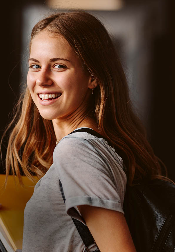 Rear view of beautiful girl walking through university hallway looking back and smiling. female student going for the lecture.
