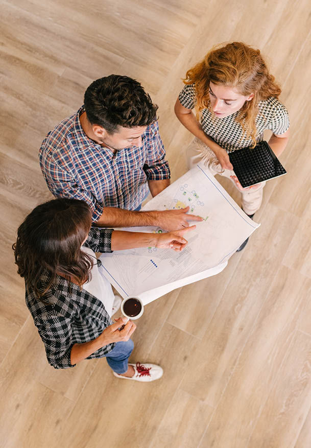 Creative architects on casual meeting reviewing blueprints standing on a wooden floor. Top view.