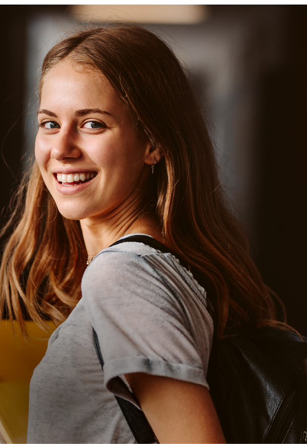 Rear view of beautiful girl walking through university hallway looking back and smiling. female student going for the lecture.